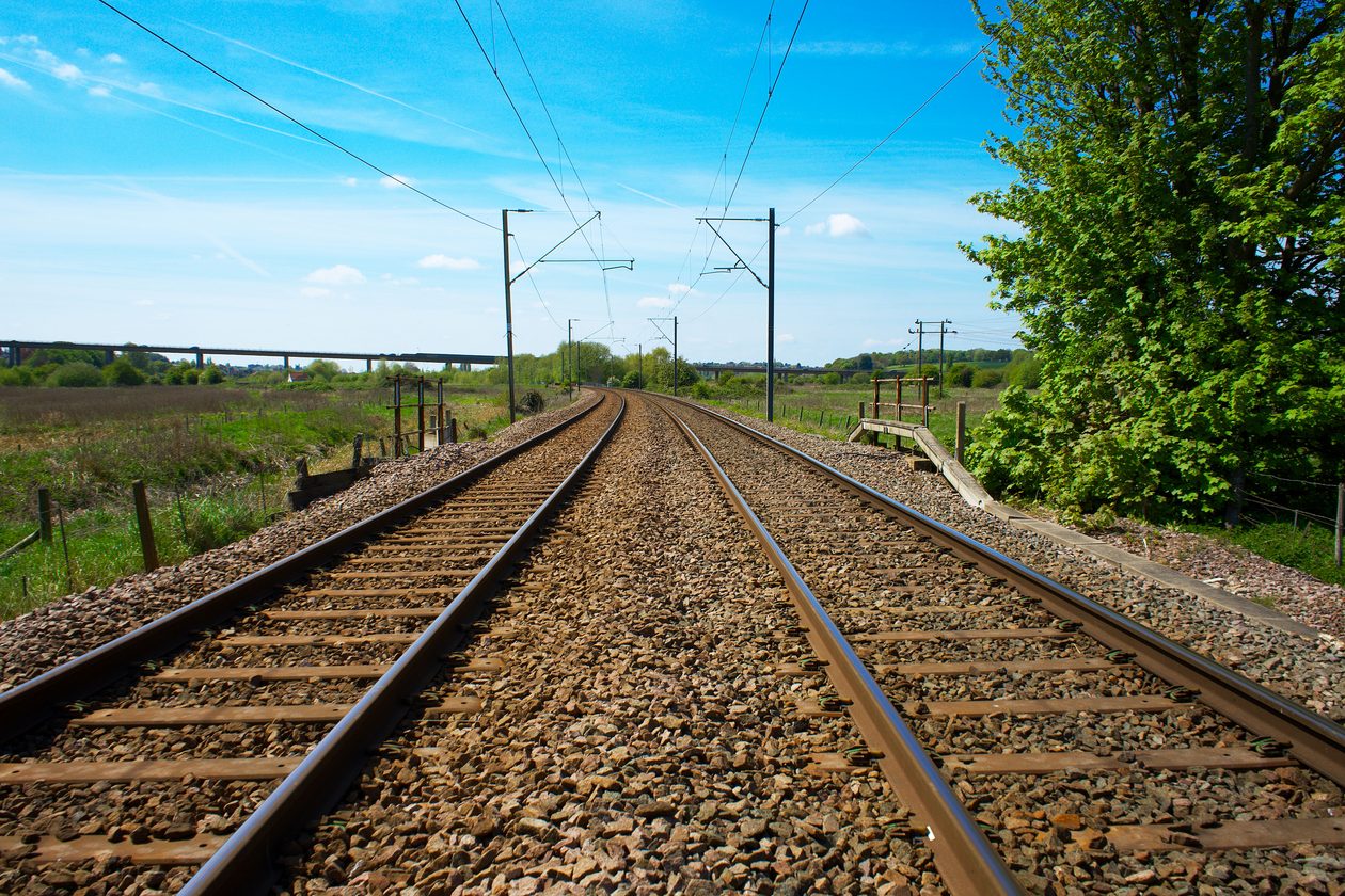 View of railway tracks stretching through the lush green UK countryside under a clear blue sky.